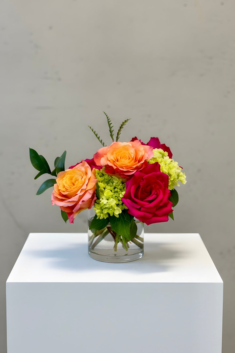Petite Treat size Sunset Spark bouquet featuring hot pink roses, coral roses, and green hydrangea in a compact modern arrangement.