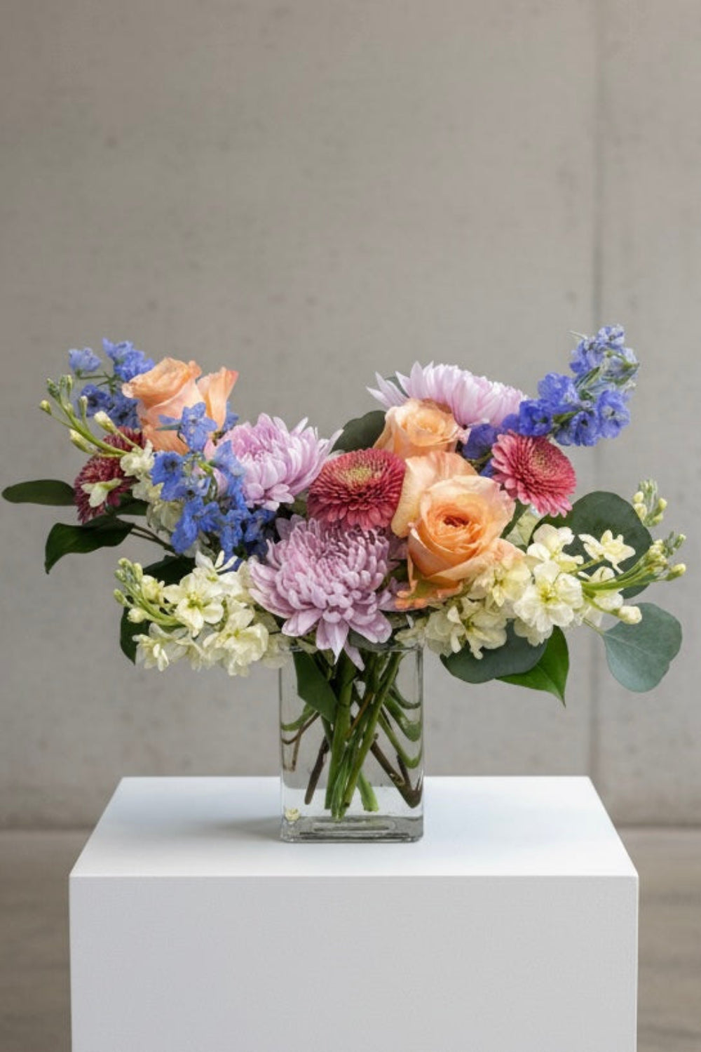 Floral arrangement in a clear vase on a white pedestal against a gray background Hand-delivered pastel bouquet from woman-owned Castle Pines florist