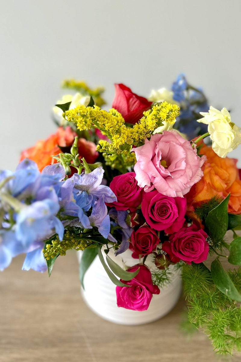 Colorful flower arrangement in a white vase on a wooden surface with a light gray background hostess gift or party decor dependably delivered in lone tree colorado