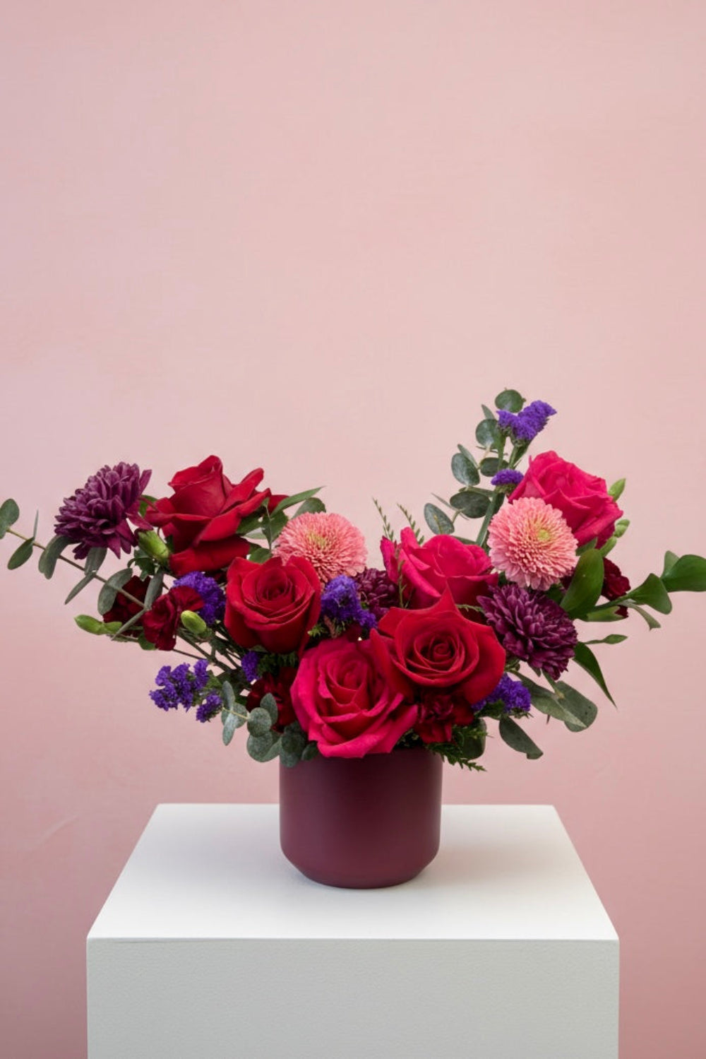 Valentine Color Crush bouquet with red roses, hot pink roses, purple cremones, pink germinis, statice, and red pixie carnations arranged in a glass vase.