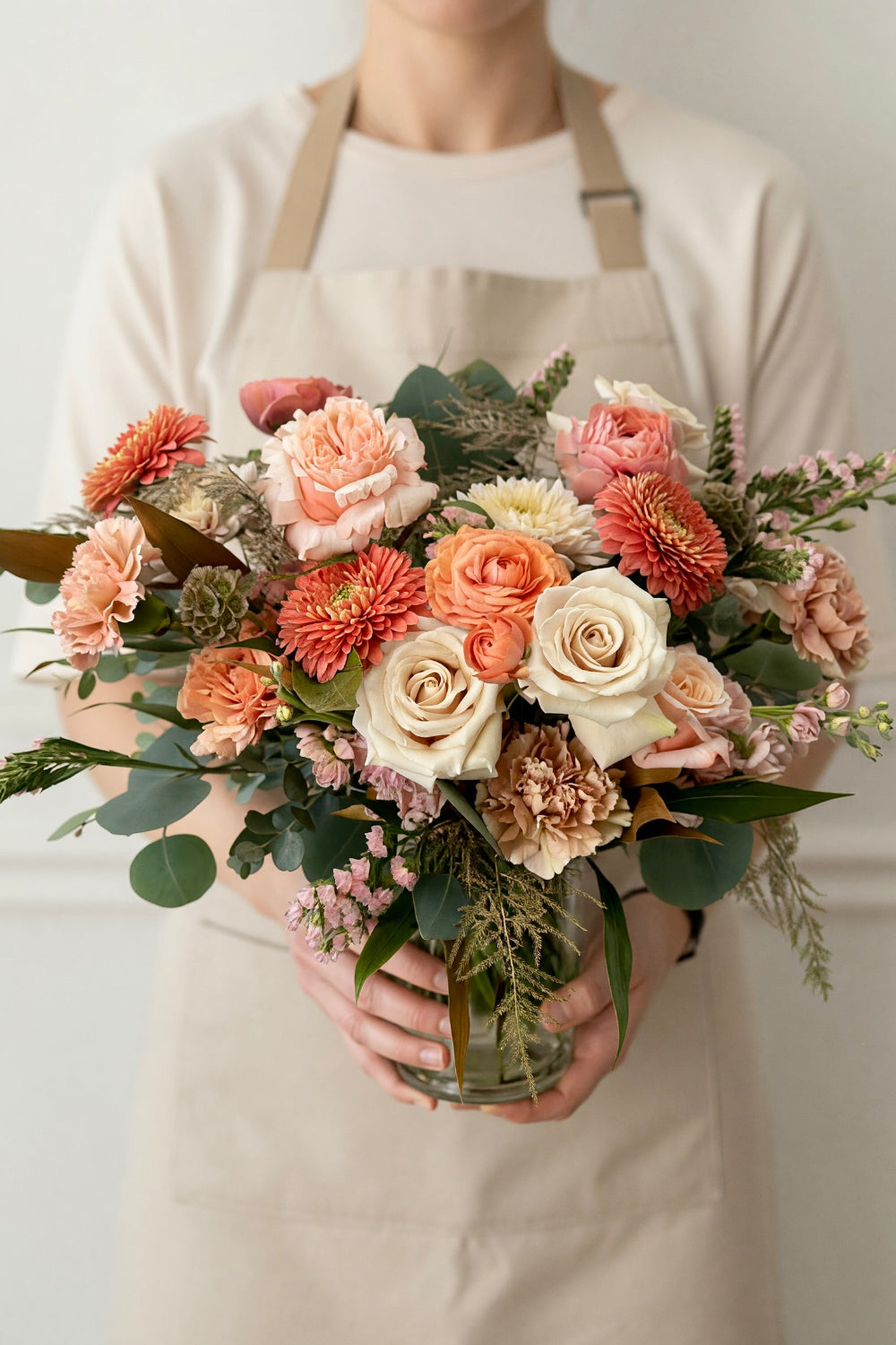 Florist holding the Classic Warm Embrace arrangement in peach and coral tones