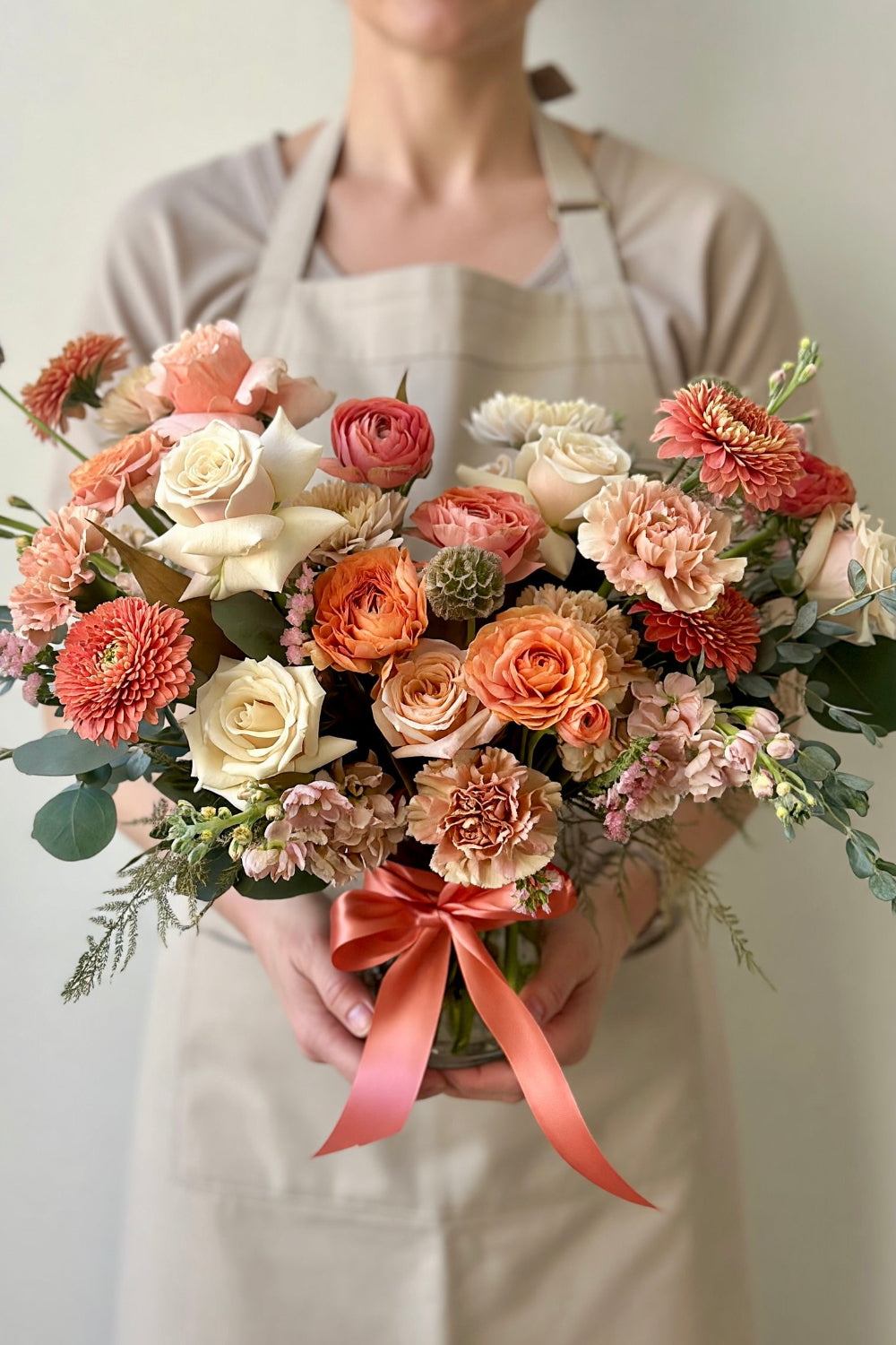  Florist holding the Premium Warm Embrace bouquet with peach, coral, and caramel flowers
