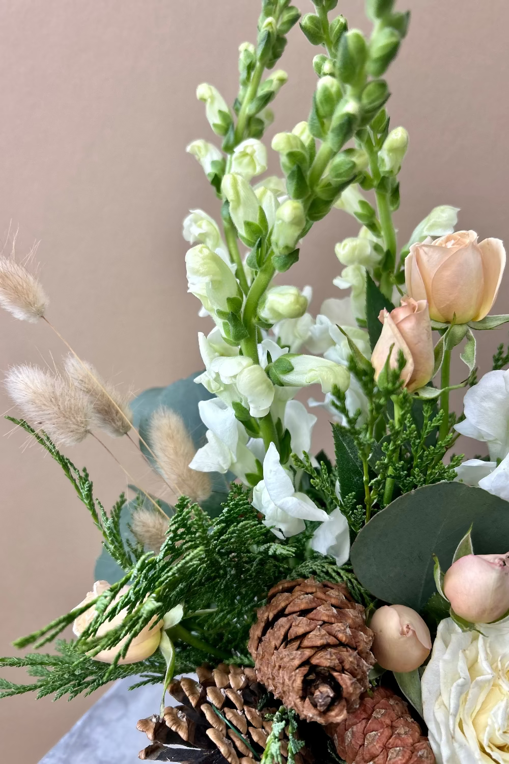 Close‑up of Winter Whisper Bouquet showing premium orchids, white rose, tan spray roses, and snapdragons with pinecone accents in birch vase