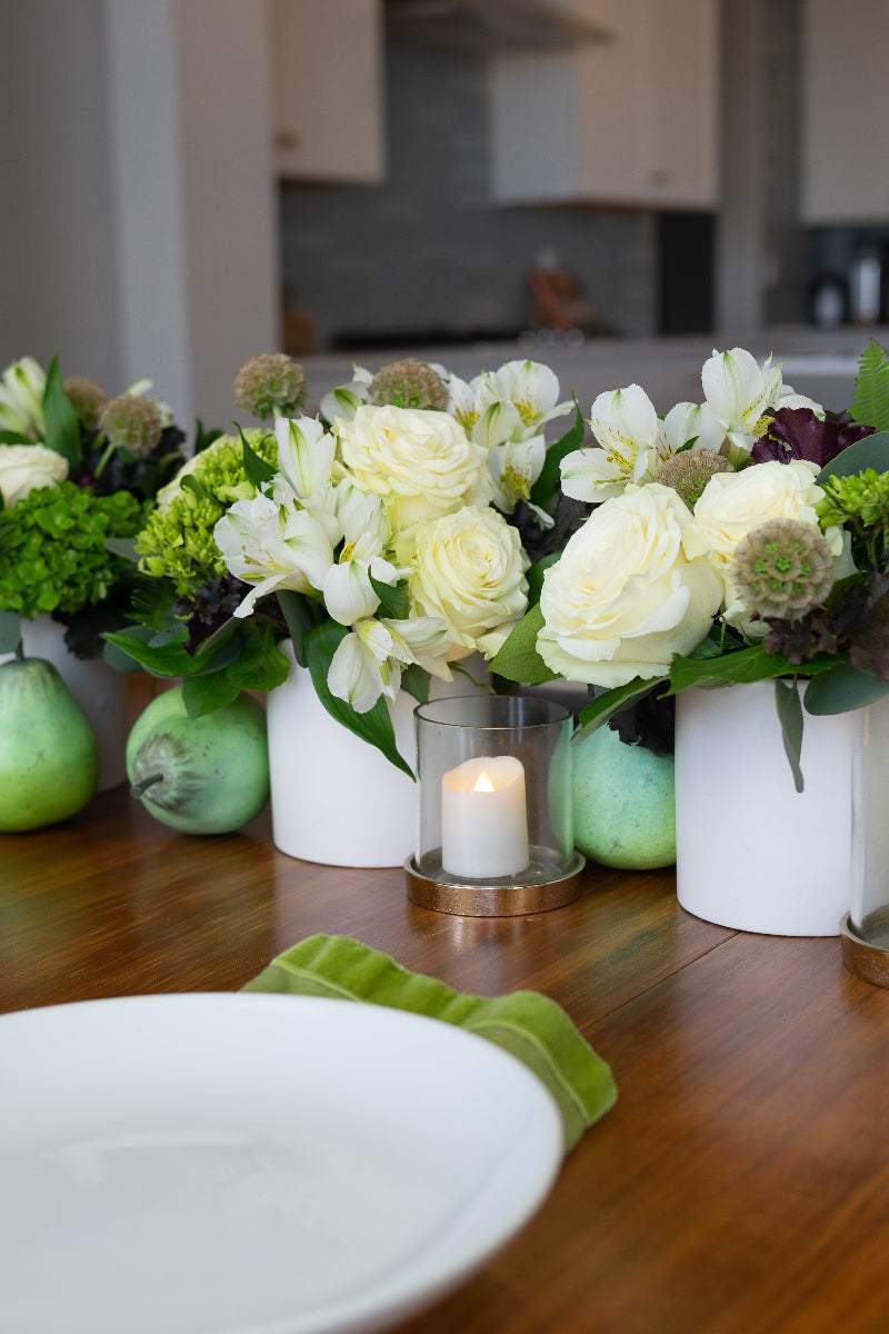 Decorative table setting with flowers, candles, and greenery in a kitchen.