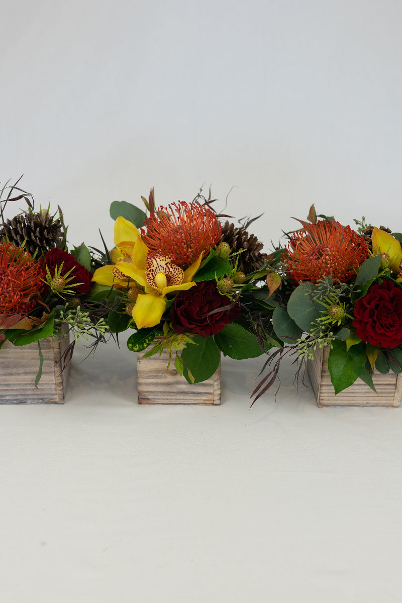 Three wooden table centerpieces with a mix of dried flowers including roses, orchids, and other foliage.