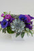 A floral arrangement featuring purple flowers and succulents in a matte white container.